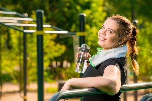 portrait of a happy fat woman with a bottle of water next to a simulator in the park