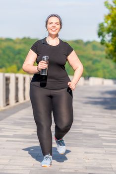 girl plus size with a bottle of water during a morning jog in the city park