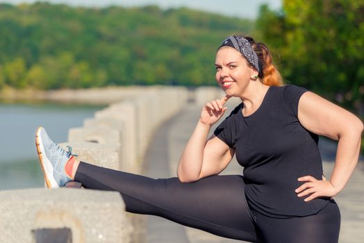 woman portrait plus size performs stretching exercises on the embankment in a city park in the early morning
