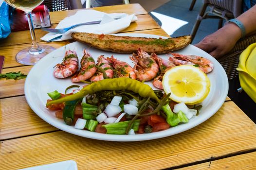 Plate of roasted prawns with slices of bread in the middle and tomatoes on a wooden table