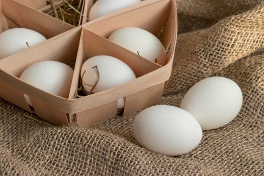 Close-up view of white chicken eggs in ecological packaging with hay or straw on sackcloth in a rustic style