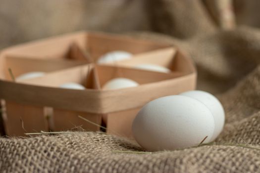 Close-up view of white chicken eggs in ecological packaging with hay or straw on sackcloth in a rustic style