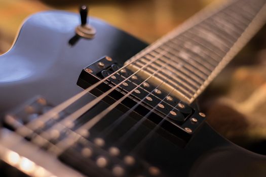 Fragment of the black electric guitar deck, pickup, neck and strings. Warm tones