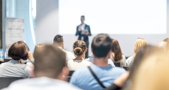 Male speaker giving a talk in conference hall at business event. Audience at the conference hall. Business and Entrepreneurship concept. Focus on unrecognizable people in audience.