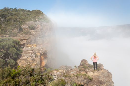 Female hiker standing on a rock pinnacle in Blue Mountains with rising fog and mist from the valley