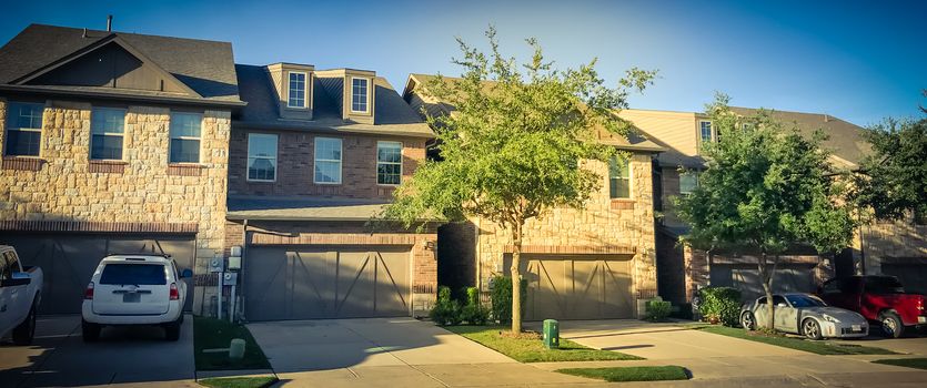 Panorama view row of brand new attached houses townhome style with double wooden garage doors and small front yard. Townhouse units outside Dallas, Texas, USA. Two stories house nice trim landscape