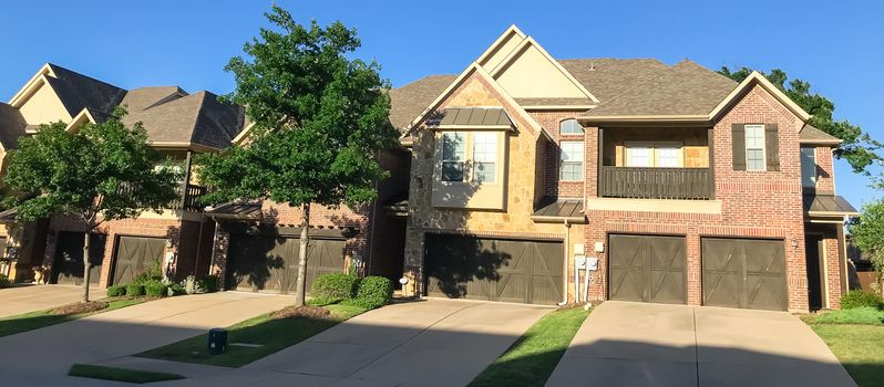 Panorama view row of brand new attached houses townhome style with double wooden garage doors and small front yard. Townhouse units outside Dallas, Texas, USA. Two stories house nice trim landscape