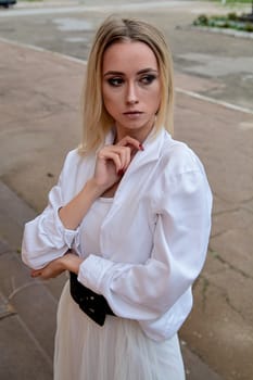 Young blonde woman dreses in white skirt and shirt posing on the steps of the old looking vintage building with large 
columns and bas-reliefs. Fashion look's woman. Young woman's modern portrait.