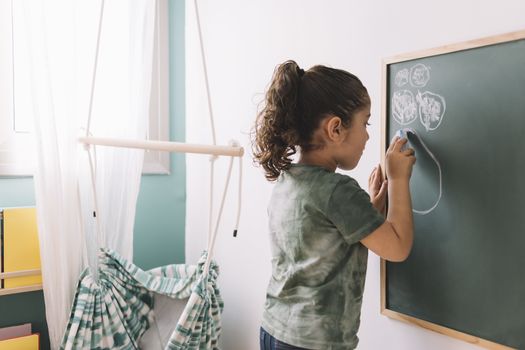 little girl drawing with a chalk on the blackboard at her room at home, copy space for text