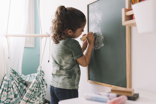 little girl drawing with a chalk on a chalkboard at her room at home, copy space for text