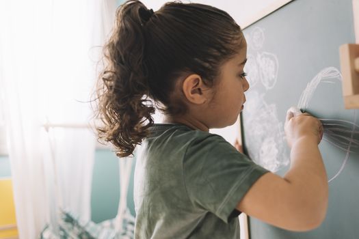 little girl drawing with a chalk on a chalkboard at her room at home, copy space for text