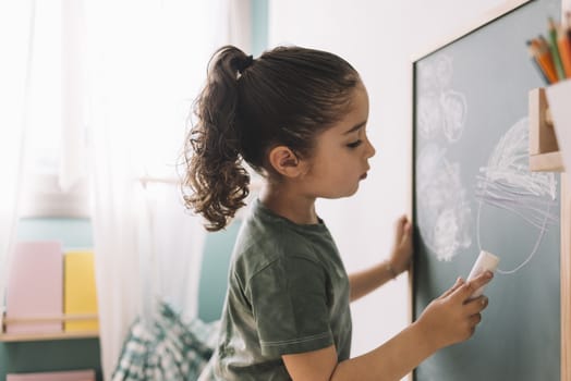 little girl drawing with a chalk on the chalkboard at her room at home, copy space for text