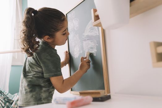 little girl drawing with a chalk on a blackboard at her room at home, copy space for text