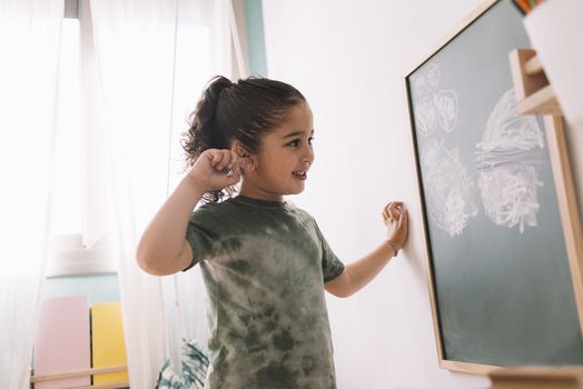 little girl smiling looking her drawing on a chalkboard at her room at home, copy space for text