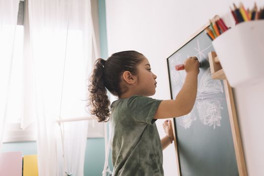 little girl drawing with a chalk on the blackboard at her room at home, copy space for text