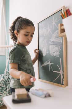 little girl picks up a chalk to draw on the blackboard at her room at home, copy space for text