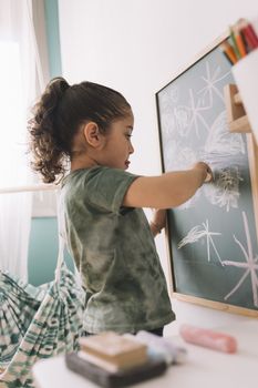 little girl concentrated drawing with a chalk on the blackboard at her room at home, copy space for text