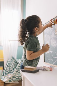 little girl drawing with a chalk on the blackboard at her room at home, copy space for text