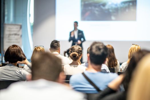 Male speaker giving a talk in conference hall at business event. Audience at the conference hall. Business and Entrepreneurship concept. Focus on unrecognizable people in audience.