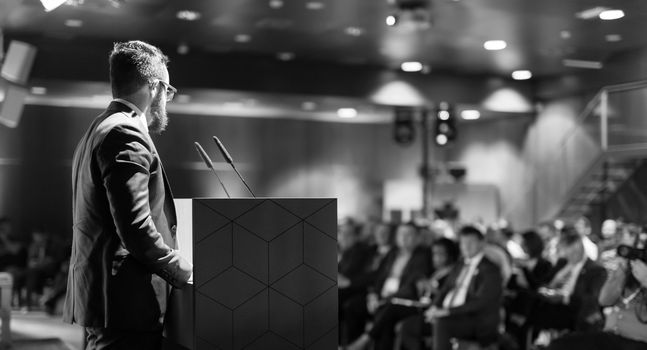 Speaker giving a talk on corporate business conference. Unrecognizable people in audience at conference hall. Business and Entrepreneurship event. Black and white image