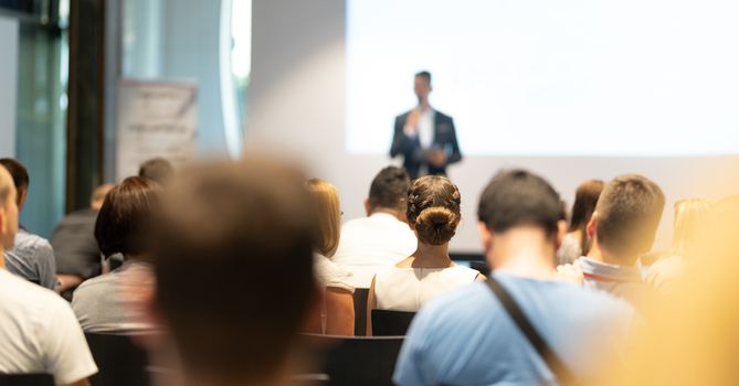 Male speaker giving a talk in conference hall at business event. Audience at the conference hall. Business and Entrepreneurship concept. Focus on unrecognizable people in audience.