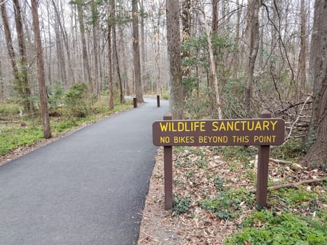 wildlife sanctuary no bikes beyond this point sign and asphalt trail or path in the forest