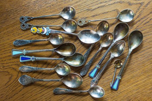 Small, antique spoons of various shapes and sizes lie on an oak table.