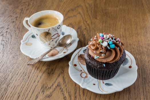 Morning, black coffee in a cup with a spoon and next to the dish is a small cream cake