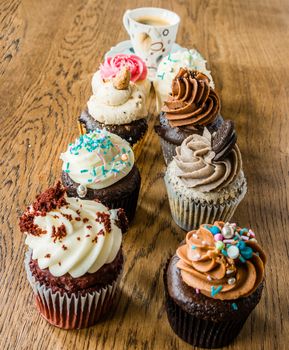 Small cupcakes with a variety of cream lined up on an oak table and black coffee in a cup