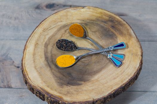 Three decorative tea spoons with turmeric, black pepper peas and red pepper lie on a wooden stand