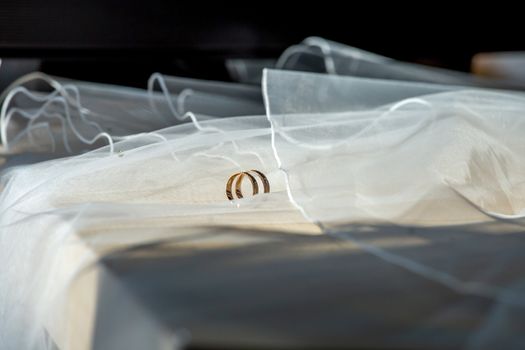 Two wedding rings on wedding veil. Gold wedding rings on the background of the white bridal veil. Rings on bridal wedding dress.