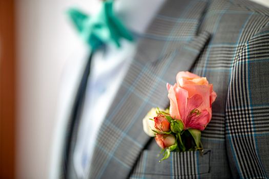 Wedding boutonniere of rose in pocket of checkered jacket of groom. Boutonniere of pink roses in the groom's pocket of jacket.