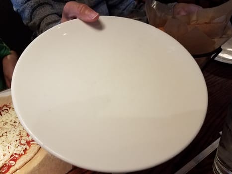 female hand holding large white plate and pizza with cheese