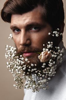 Creative Portrait of young beautiful man with a beard decorated with flowers.