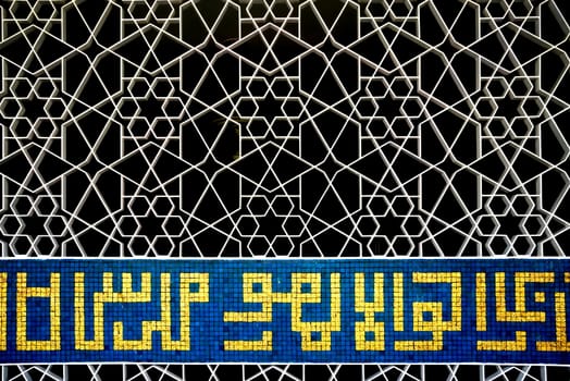 white Islamic star pattern metallic door with yellow and blue mosaic calligraphy with black background
