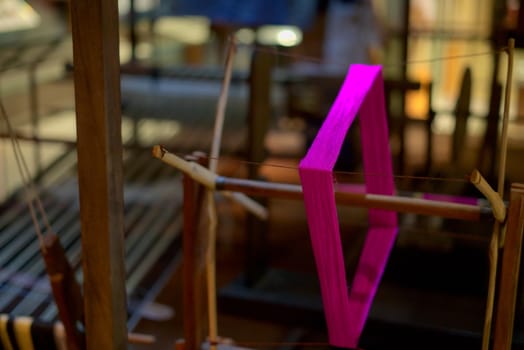 Malaysian traditional textile wooden loom with flashy spinning purple thread in focus