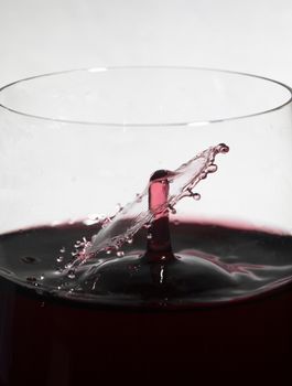 Falling wine drop collides with wine splashing in glass, creating a splash ring.