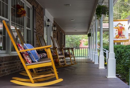 Rocking chairs lined up on long front porch. Red barn is in the background.