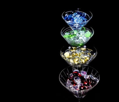 Colorful beads in a line of martini glasses against a black background. Glasses are lit from above.