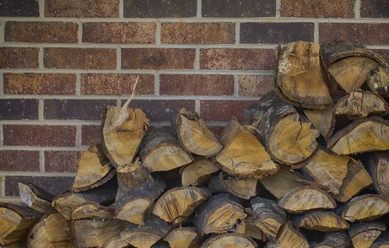 Color view of split and stacked oak firewood against a brick wall.