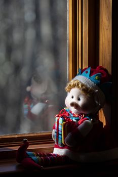 Christmas elf sits in the sun on a window sill.