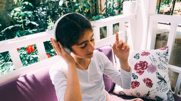 She seats outside in the garden, wearing headphones.