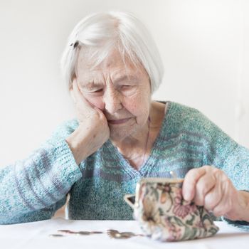 Elderly 96 years old woman sitting miserably at the table at home and counting remaining coins from pension in her wallet after paying bills. Unsustainability of social transfers and pension system.