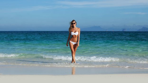 Pretty smiling girl in bikini walking at tropical sea beach