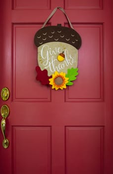 Fall-themed decoration hangs on red entrance door with brass handle.