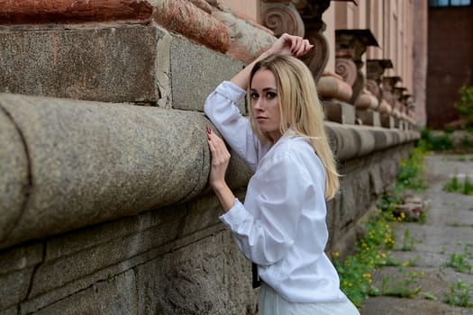 Young blonde woman in white skirt and shirt near the wall of the old looking vintage building. Fashion woman. Young woman's modern portrait.