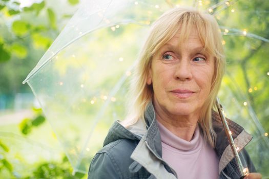 Portrait of beautiful senior woman with transparent umbrella with light bokeh background