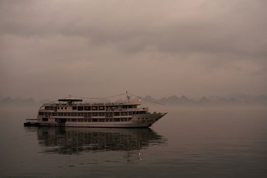 one cruise boat on Halong bay cloudy early light with myst and reflection