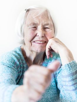 Content 96 years old elderly woman giving a thumb up and looking at camera. Focus on the womans face, thumb out of focus. Old age and the quality of life concept.