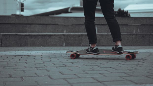 Woman skateboarder legs skateboarding at grey city